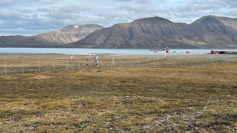 Målestasjon, tundra, gjerder og rullebane i forkant av fjord og fjell.