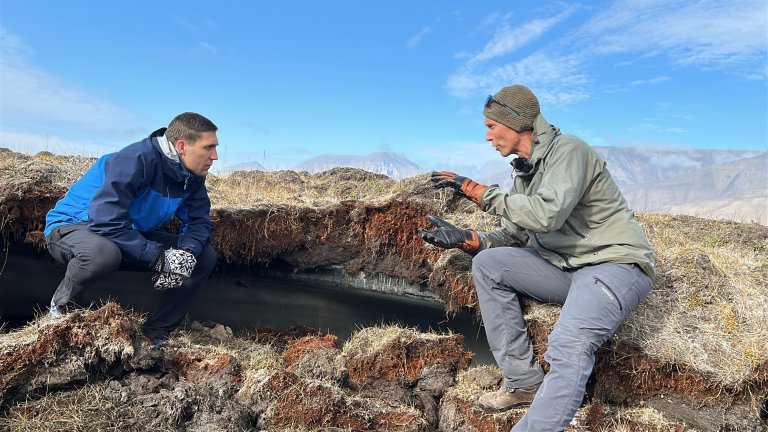 Ministeren og forskeren sitter bøyd mens de titter inn i sprukken permafrost.