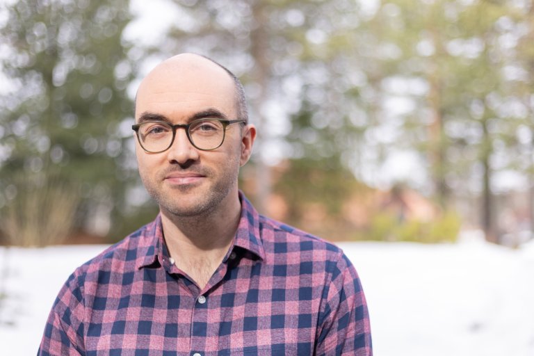 Portrett av Matthew Simpson, briller og rutete skjorte, eksteriørbilde med dus skog i bakgrunnen.