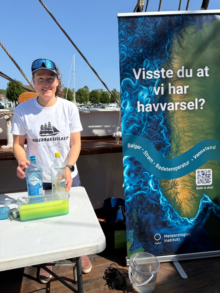 En dame står ute foran et bord, solbiller og caps på hodet, en roll-up i bakgrunnen: "visste du at vi har havvarsler?"