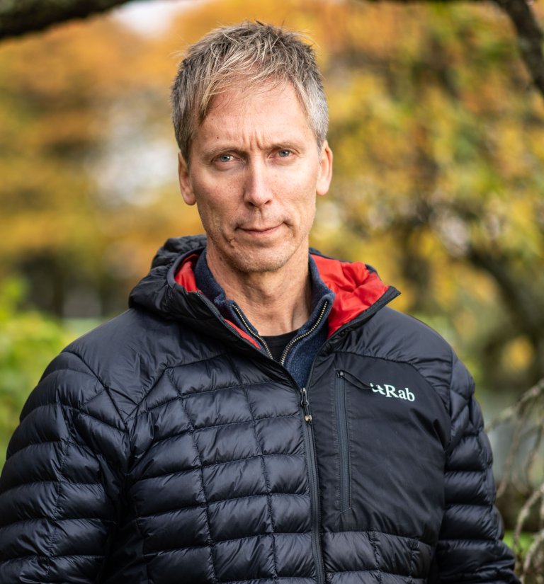 Halvportrett av alvorlig mann med mørk dunjakke, ute.