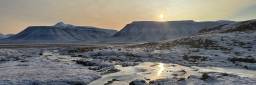 Lav sol over et delvis frossent slettelandskap på Svalbard.