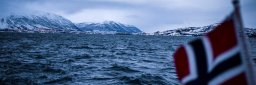 Fjell og hav i vintermørket, med norsk flagg i forgrunnen